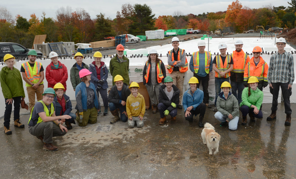 Treehouse Village members and professionals from Tate Engineering wearing hardhats pose for a photo after a day of assembling the styrofoam forms for the insulated concrete form walls of their common house. A dog joined the photo op.