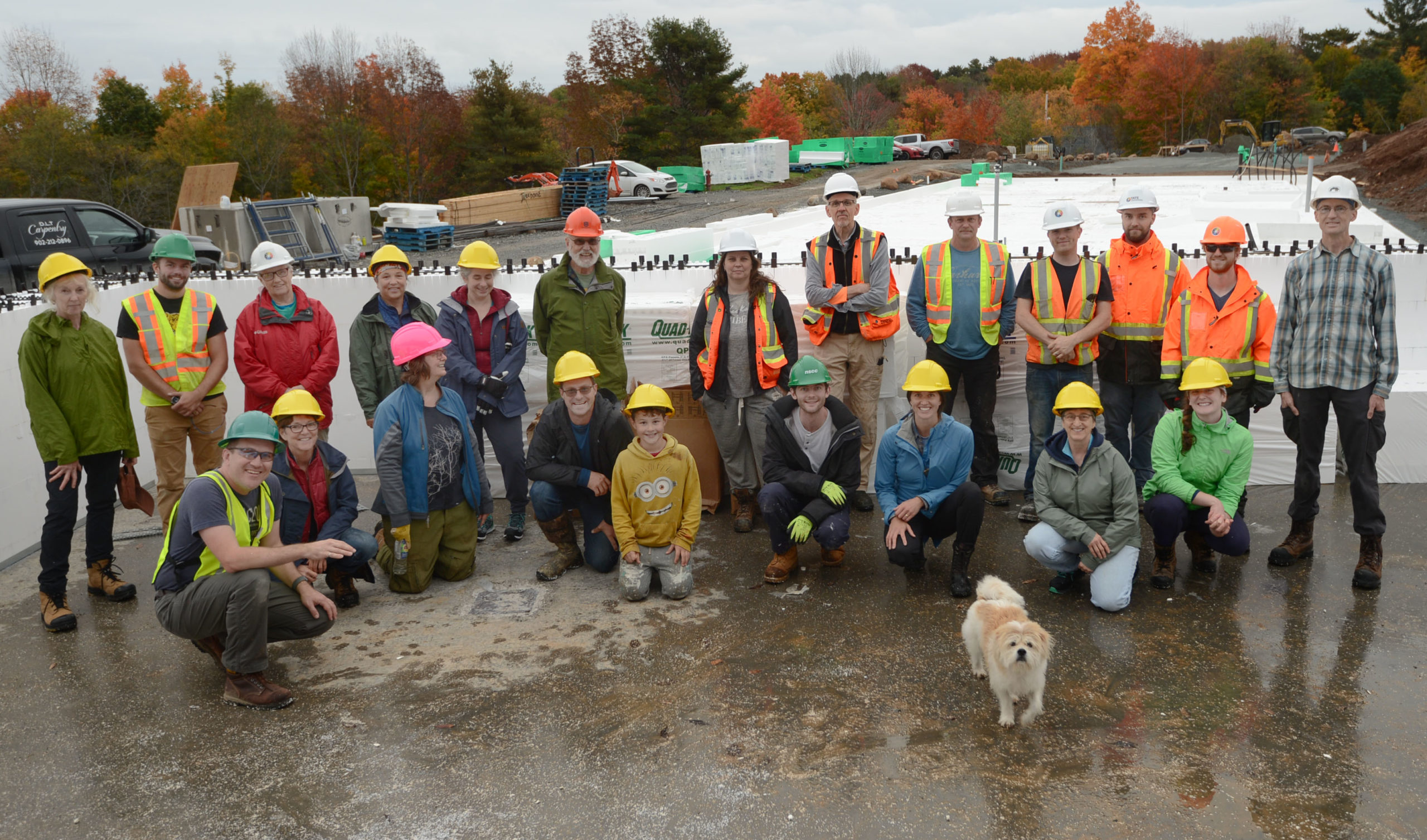 Treehouse Village members and professionals from Tate Engineering wearing hardhats pose for a photo after a day of assembling the styrofoam forms for the insulated concrete form walls of their common house. A dog joined the photo op.